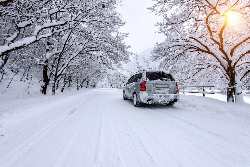 Car and falling snow in winter on forest road with much snow.