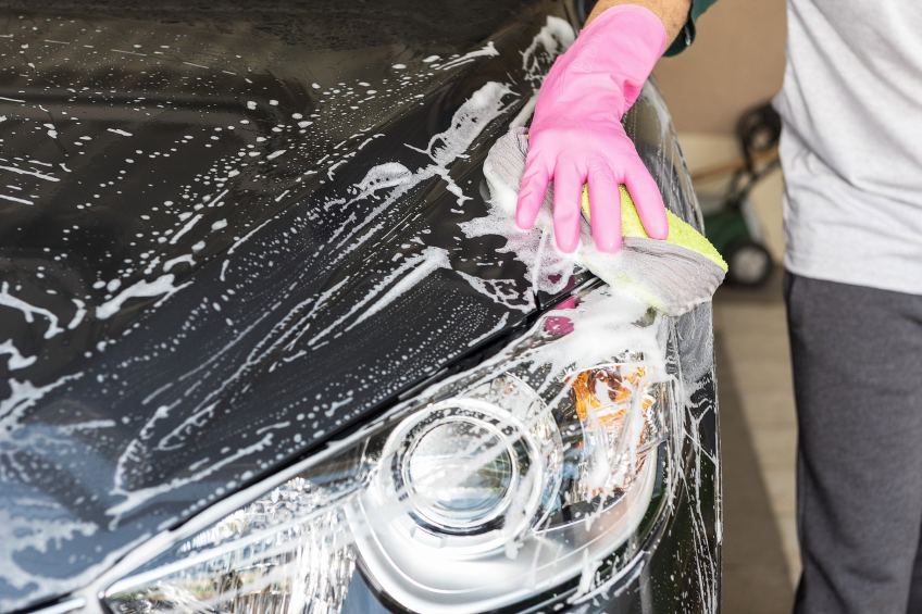 Person with pink glove hand washing car with soap and sponge