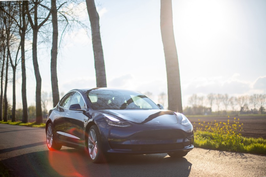 Tesla driving down a sunny road with trees.